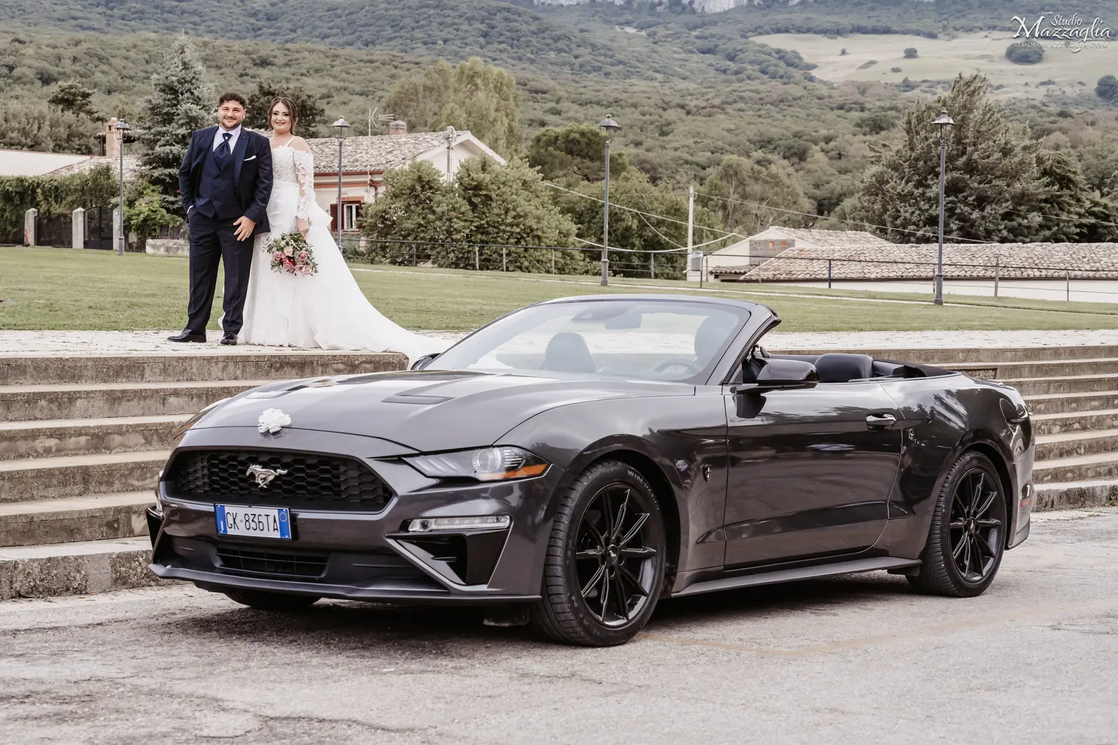 Sposi posano accanto a una Mustang cabrio grigia davanti alla monumentale scalinata in pietra di Ficuzza a Corleone.
