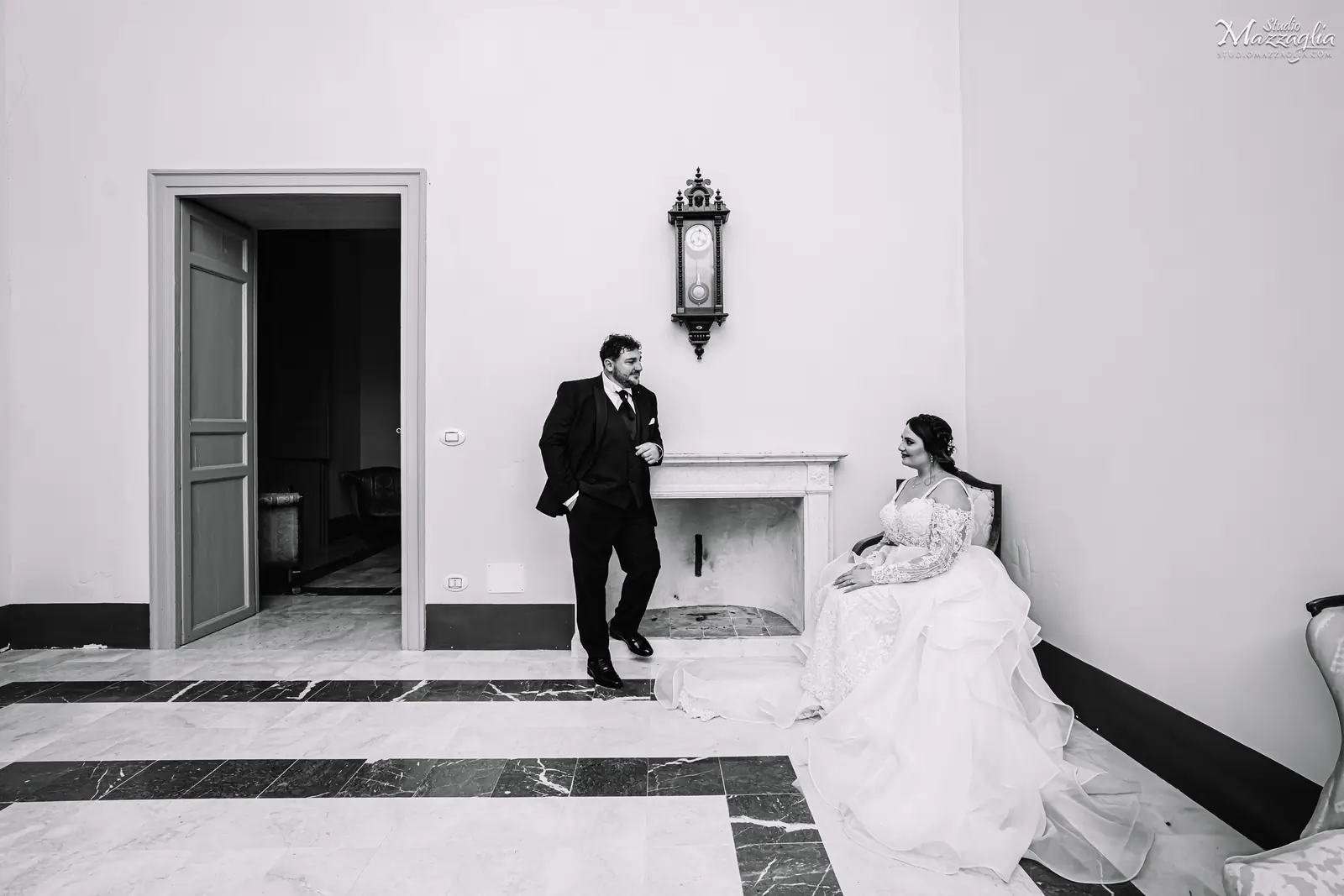 Ritratto nuziale artistico in bianco e nero con la sposa seduta e lo sposo accanto a un camino antico in una dimora storica a Palermo.