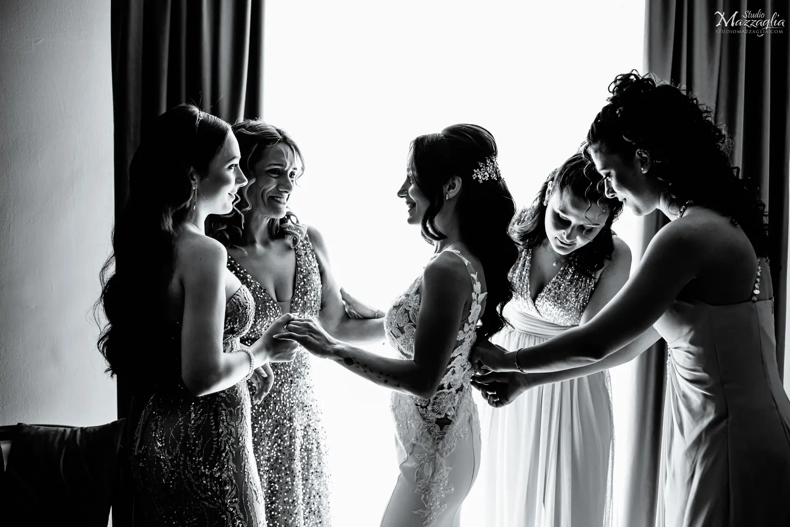 La sposa e le damigelle Scatto in bianco e nero della sposa circondata dalle sue testimoni e amiche mentre la aiutano con i preparativi finali.