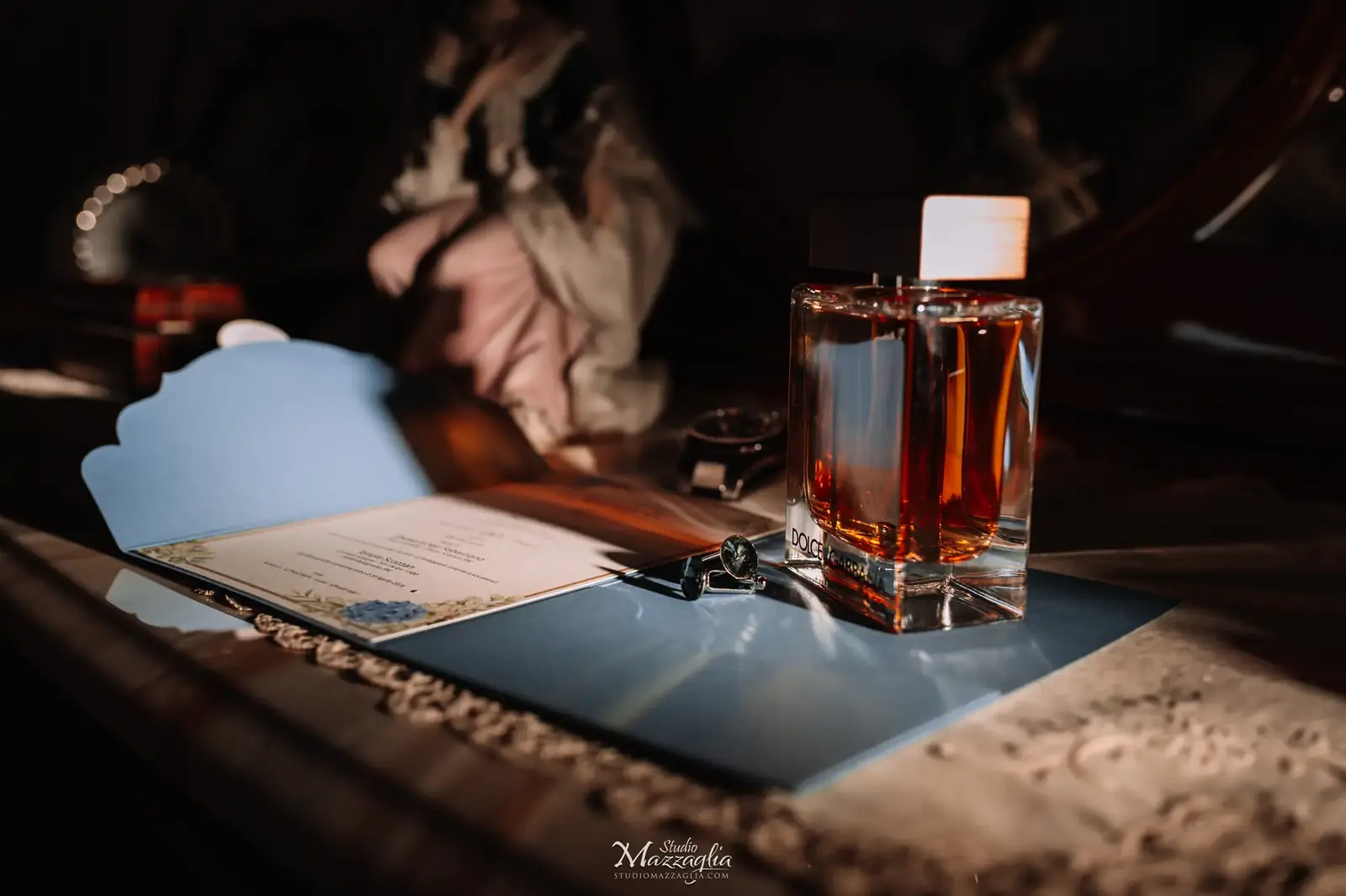 Fotografia artistica di still life dei dettagli dello sposo, con profumo Dolce e Gabbana, gemelli da camicia e invito di nozze su tavolo antico.